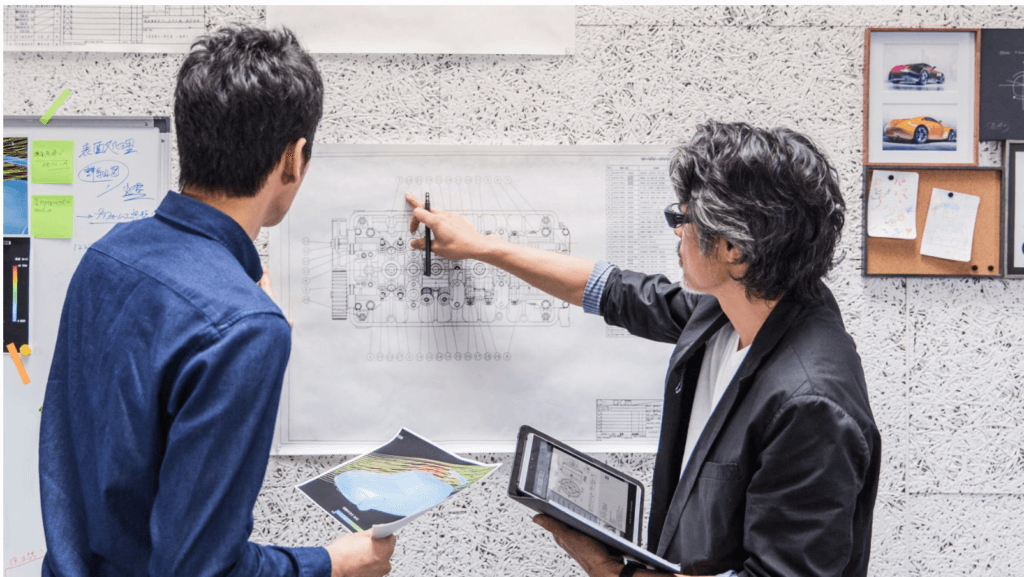 Two people are looking at a wall with plans on it.