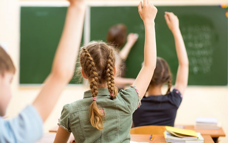 A group of children raising their hands in front of a chalkboard.